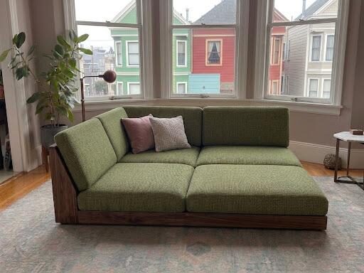 Low walnut-framed sofa with green cushions by the window